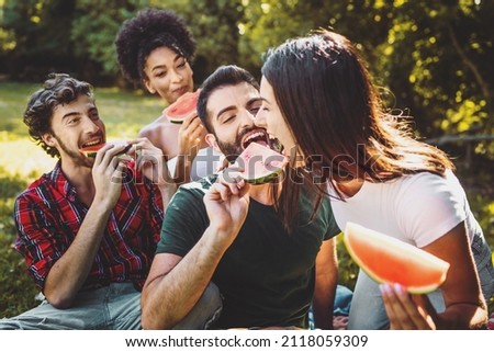 Picnic in the countryside. Group of young friends, on spring day are sitting on the ground in a park under the trees - eating healthy watermelon slices and joking together