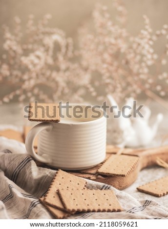 A white ceramic mug with milk, biscuits and a white ceramic bunny surrounded by small white flowers. A gentle breakfast in a light key