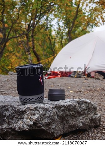 A pot for a gas burner with a mug sits on a stone against the background of a tent. photo