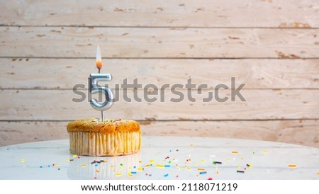 Happy birthday greetings for 5 years from silver numbers on the background of white boards copy space. Beautiful birthday card with a muffin with a burning candle for five years