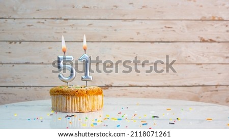 Happy birthday greetings for 51 years old from silver numbers against the background of white planks of mine space. Beautiful birthday card with a muffin with a burning candle for fifty one years