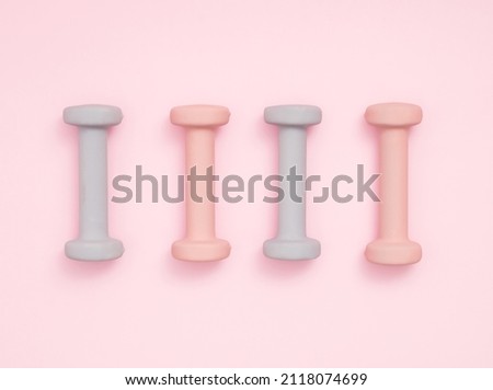 Four pastel color exercise weights on pastel pink background with soft shadow. Exercise, healty lifestyle or New Year resolution concept. Flat lay.