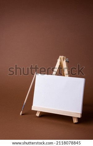 White canvas on a small wooden easel stand minimal concept on the brown backdrop. Empty blank mock up frame for design with copy space.
