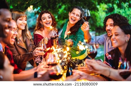 Happy friends having fun with fire sparkles while toasting red wine - Young millenial people camping at summer picnic barbecue party on night mood - Youth life style concept on warm vivid filter