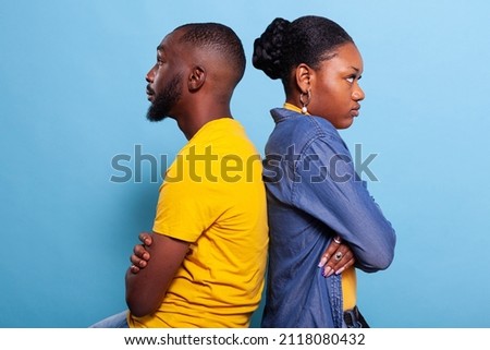 Angry partners sitting back to back with arms crossed in studio. Irritated boyfriend and girlfriend with relationship problems and argument fighting in front of camera. Distant upset couple Royalty-Free Stock Photo #2118080432