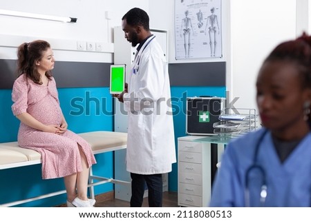 Adult with pregnancy looking at tablet with vertical green screen in office. General practitioner holding device with isolated template and mockup background for chroma key on display.