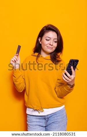 Modern adult holding credit card to make purchase online with smartphone. Positive woman using internet banking and money to do shopping payment on mobile phone. Person buying on sale