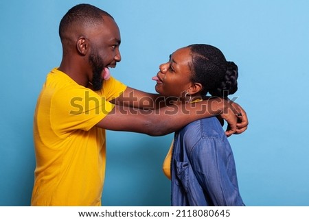 Playful lovers hugging and sticking tongue out at each other. Girlfriend and boyfriend fooling around with goofy gesture, expressing happiness and corny romance. Positive couple having fun. Royalty-Free Stock Photo #2118080645