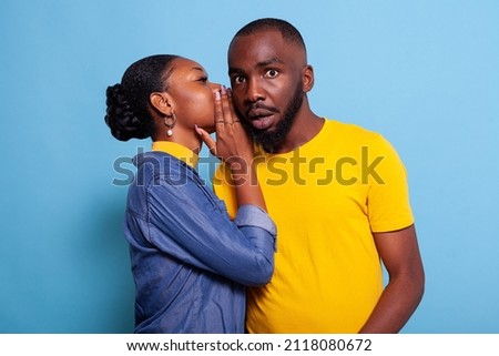 Astonished man finding out secret rumour from girlfriend in studio. Young woman whispering gossip in ear of boyfriend, having confidential conversation. Curious person listening to mistery. Royalty-Free Stock Photo #2118080672