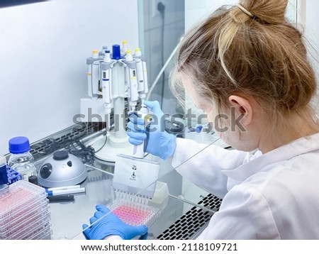 A female PhD student performing a biological experiment on a cancer cells in a sterile environment of designated biosafety laboratory at research facility.  Royalty-Free Stock Photo #2118109721