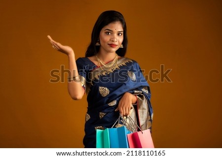 Beautiful Indian young girl or woman holding and posing with shopping bags on a brown background