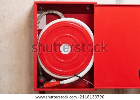 Red fire hose reel, mounted on a concrete wall background.