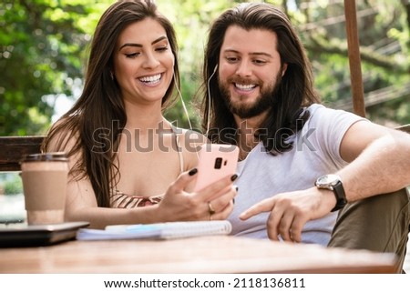 brazilian couple watching video on mobile phone with headphones in the park