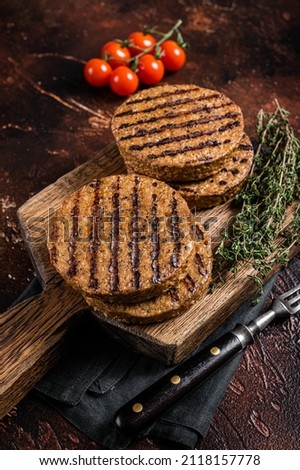 BBQ Grilled plant based meat burger patties, vegan cutlets on wooden board with herbs. Dark background. Top view