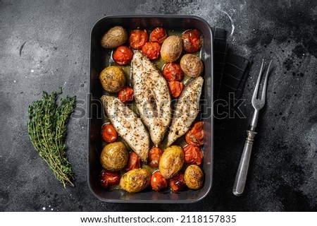 Roasted halibut fish steaks with tomato and potato. Black background. Top view