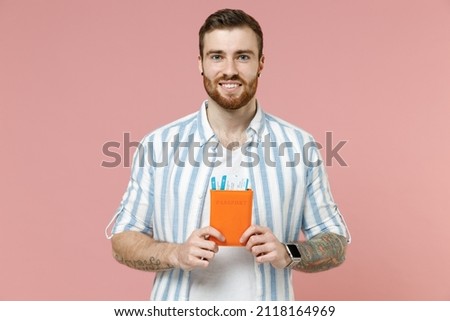 Traveler tourist man 20s in striped shirt hold passport tickets isolated on pastel pink color background. Passenger travel abroad on weekends getaway. Air flight journey concept. Tattoo translate fun.
