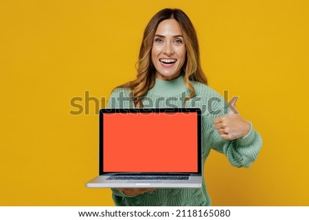 Young woman 30s in green knitted sweater hold use work on laptop pc computer with blank screen workspace area show thumb up gesture isolated on plain yellow color background. People lifestyle concept