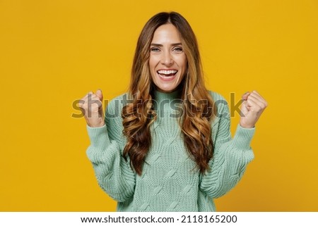 Young fun caucasian woman 30s wearing green knitted sweater doing winner gesture celebrate clenching fists say yes isolated on plain yellow color background studio portrait. People lifestyle concept Royalty-Free Stock Photo #2118165200