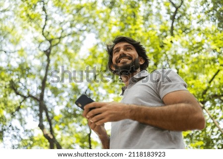 View of young man using a smartphone at day time with a green park in the background. Mobile phone, technology, urban concept. High quality photo
