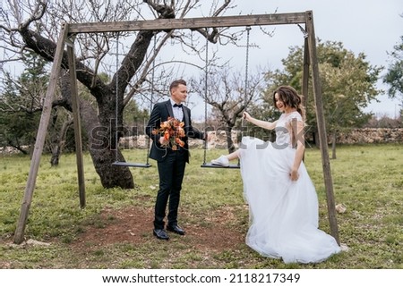 Happy stylish smiling couple walking in Tuscany, Italy on their wedding day. NEWLYWEDS WITH THE SWING IN THE PARK. The bride and groom walk down the street by the hands. A stylish young couple walks Royalty-Free Stock Photo #2118217349