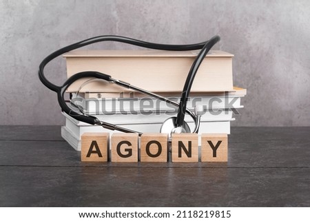 agony word written on wooden blocks and stethoscope on black background. healthcare conceptual for hospital, clinic and medical busines