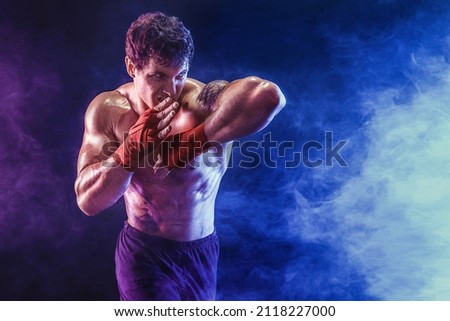 Portrait of muscular kickboxer who delivering an elbow hit isolated on smoke background. The concept of sports, mixed martial arts. Mixed media. Royalty-Free Stock Photo #2118227000