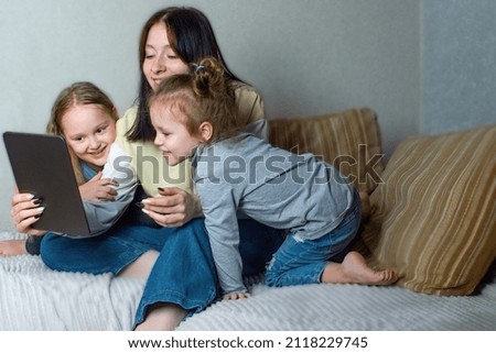 The older sister is talking and watching something interesting on the tablet, the younger two sisters are interested in watching what is on the screen of the gadget. Family fun at home