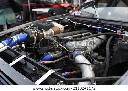 Sports car engine with turbine. An open race car hood on a pit stop while racing on a race track. Motor with turbocharger. Boos and tunning. Royalty-Free Stock Photo #2118241172