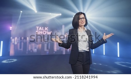 Happy presenter in a suit and glasses running onto the stage and announcing the start of the famous comedy, late-night show in an illuminated room with LED screen and 3D inscription Royalty-Free Stock Photo #2118241994