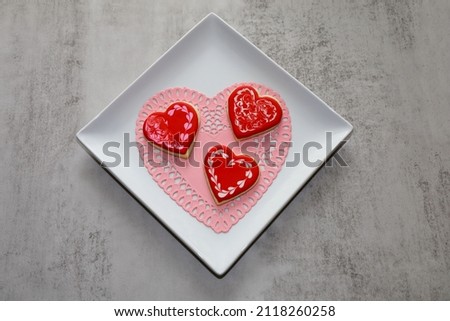 Heart shaped sugar cookies with royal icing on a white plate lined with a pink heart doily.