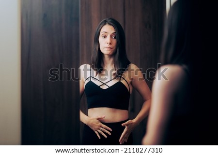 
Insecure Self-conscious Woman Checking her Body in the Mirror. Girl feeling bloated looking at her stomach in mirror reflection 
 Royalty-Free Stock Photo #2118277310