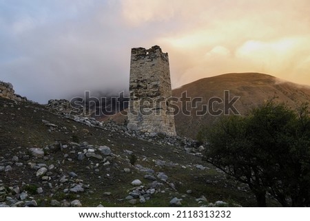 A old Ossetian battle tower against the background of sunset in foggy mountains. Verhniy Fiagdon. Northern Ossetia, Russia