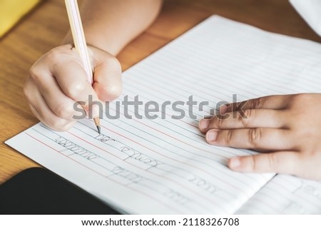The kid's hand is practicing writing English cursive handwriting sentences in a notebook with a pencil. Cursive handwriting practice.  Kindergarten writing skills. Self-learning. Copy space for text. Royalty-Free Stock Photo #2118326708