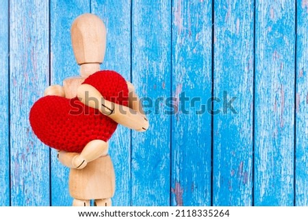wooden man with a red heart in his hands on a blue background. High quality photo