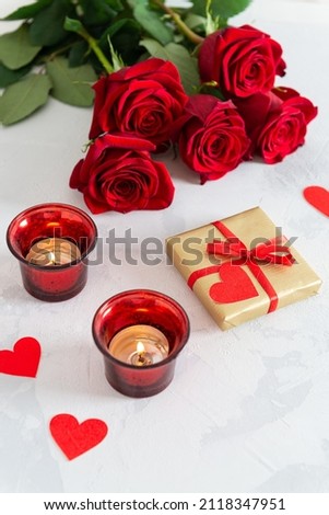St. Valentine's Day background. Small hearts, candles, a gift box and red roses bouquet on light concrete background. Romantic love background. Happy Valentines Day. Greeting card, poster.