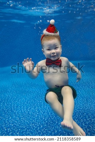 baby boy in a Santa Claus hat dives underwater in the pool with pleasure. Christmas picture. 