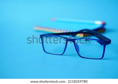 notepad, eyeglass and a pencil on blue background 