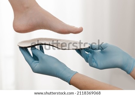 Orthopedic insole on a white background. Hands in rubber gloves hold an orthopedic insole. Foot care, comfort for the feet. Doctor orthopedist tests the medical device. Flat feet correction. Royalty-Free Stock Photo #2118369068
