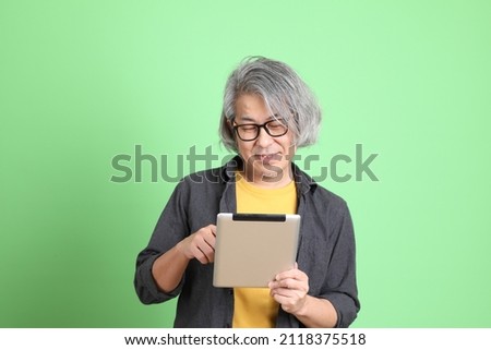 The senior Asian man with smart casual dressed standing against the light green background.