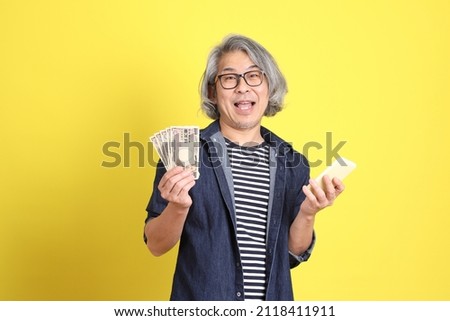 The senior Asian man with jean dressed standing against the yellow background.