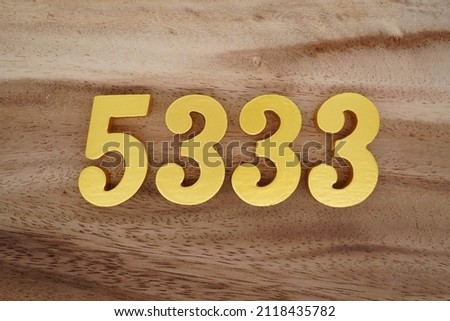 Wooden Arabic numerals 5333 painted in gold on a dark brown and white patterned plank background.