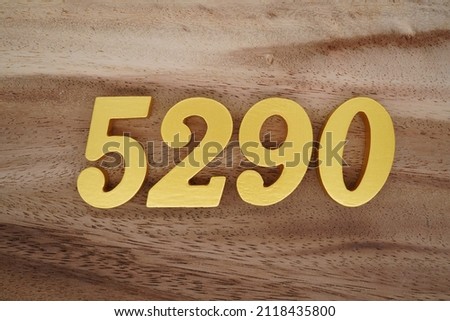 Wooden Arabic numerals 5290 painted in gold on a dark brown and white patterned plank background.