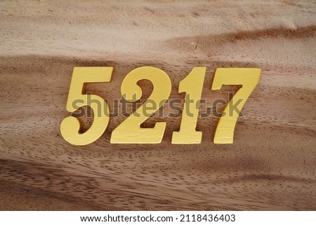 Wooden Arabic numerals 5217 painted in gold on a dark brown and white patterned plank background.
