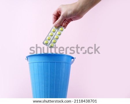 Hand throwing pills away, trash bin with pills and blisters inside, medecine in trashcan, pharmaceutical waste, expired medicines concept, closeup Royalty-Free Stock Photo #2118438701