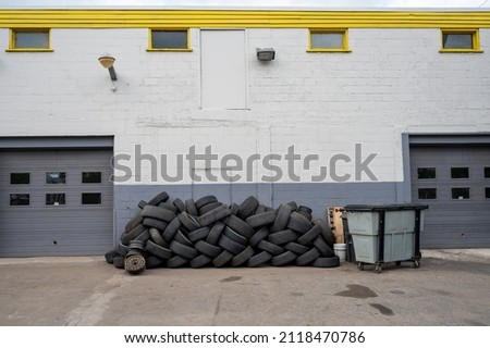 A pile of used tires sits well organized behind an industrial building. Royalty-Free Stock Photo #2118470786