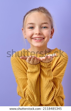 cute girl blowing a kiss. pretty young child sending love. romance and warm feelings concept. portrait on purple studio background. portrait of caucasian american child in casual yellow shirt