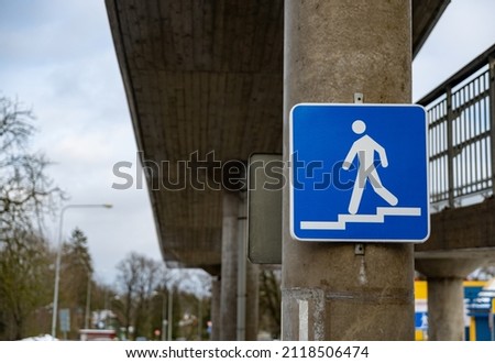Blue pedestrian sign on a concrete pole under a pedestrian bridge