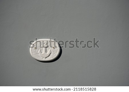 Traditional handmade clay plaque with an engraved anchor against a grey stucco wall in Limeni, Lakonia Mani, Peloponnese Greece. 