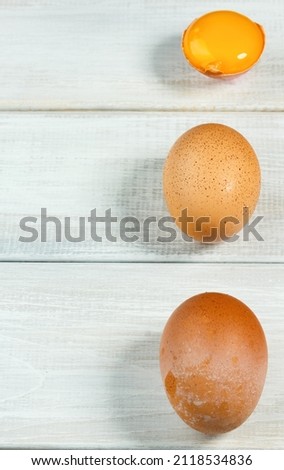 Fresh chicken eggs. Two whole brown chicken eggs and one cracked on a white wooden background. Yolk and two eggs vertically, copy space, selective focus
