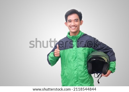 Portrait of Asian online taxi driver wearing green jacket showing thumb up hand gesture and holding helmet. Isolated image on white background Royalty-Free Stock Photo #2118544844